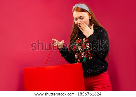 Surprised girl looking into open Xmas gift bag. Isolated on a pink background.