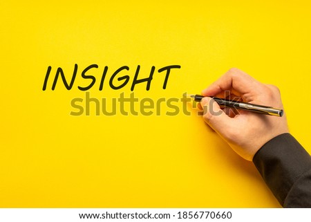 Male hand writes in black pen the word insight on a yellow background with copy space. Business concept photo