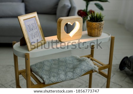 Top angle view of hand made home decor, coffee table with photo frame, decorative wooden lamp with heart picture, and green plant in wicker flower pot. Interior of living room