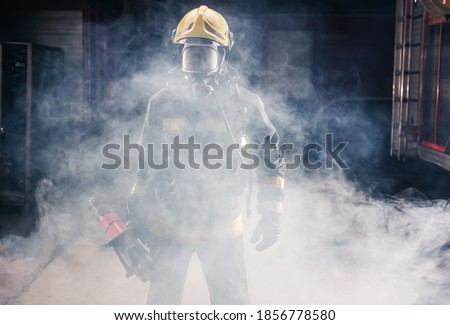 Portrait of young fireman standing and holding a chainsaw in the middle of the chainsaw's smoke