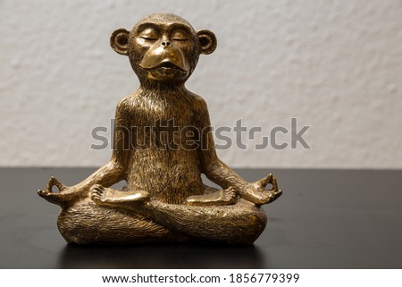 A gold colored meditating monkey statue sitting on a black surface, the background of the picture is white and blurry.
