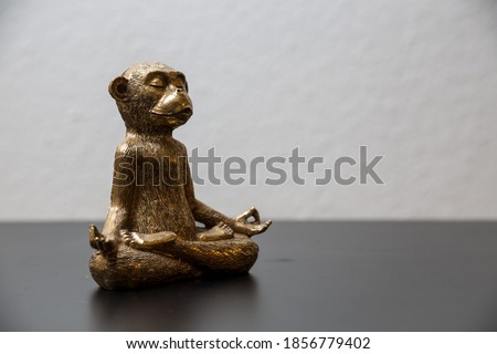 A gold colored meditating monkey statue sitting on a black surface, the background of the picture is white and blurry.