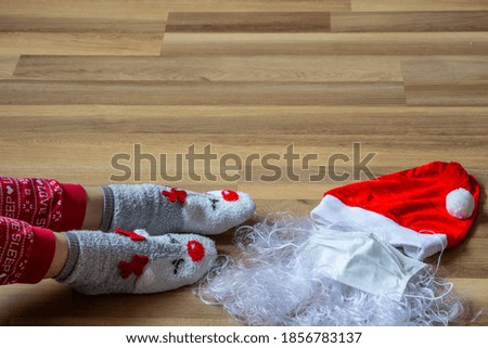 Santa hat, mittens and beard with medical mask on wooden background