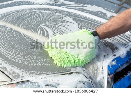 A man uses a soft, green micro fiber mitt mied with soapy water to wash his car. Royalty-Free Stock Photo #1856806429