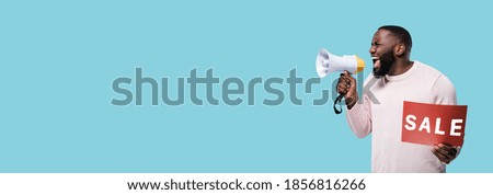Panoramic photo of African American man emotionally shouts into a megaphone and holds a red "sale" sign in his hand standing on isolated blue background. Copy space for your advertising or text