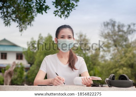 Asian women in medical mask holding pen sitting on table reading book study education, Women in mask keep social distancing protect coronavirus covid19