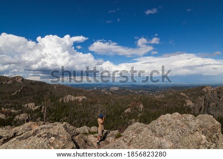 A photographer stands on a granite rock formation taking pictures with a dynamic landscape background in Custer State Park, South Dakota.