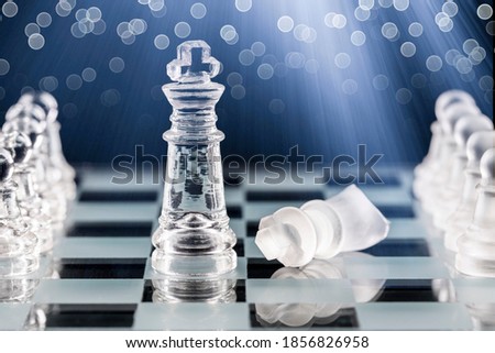 Glass chess pieces on a glass chessboard with reflection, on a blue background.