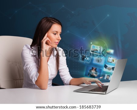 Beautiful young girl sitting at desk and watching her photo gallery on laptop