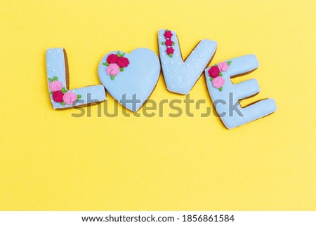Inscription Love by homemade cookies with blue icing on yellow pastel color. Love romance concept. Valentines Day background. View from above.