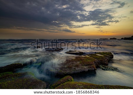 Calm ocean long exposure. Stones in mysterious mist of the sea waves. Concept of nature background. Sunset scenery background. Cloudy sky. Soft focus. Mengening beach, Bali, Indonesia.