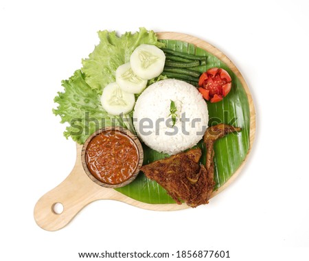 Fried chicken with ripe golden skin laid out on a wooden sheet on a white background, plus white rice, chili sauce and various vegetables, view from above. commonly used for menus and picture packs.
