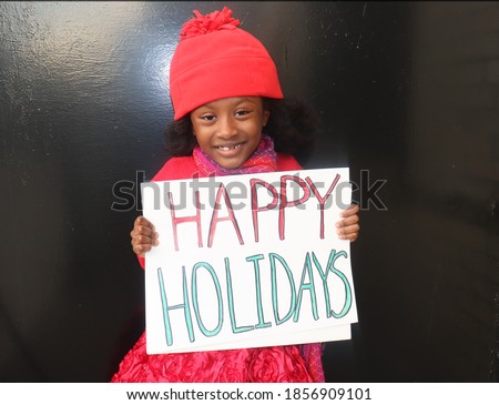 Cute Kid outside in ref winter hat holding Happy Holidays sign Christmas Colors Black background