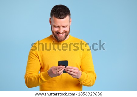 funny cheerful man in a yellow sweater with smartphone on colored blue background
