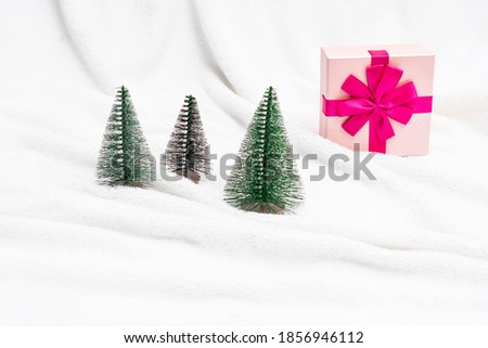 Open pink gift for New year, artificial trees on a white background, artificial snow, copy space. Concept of the winter holidays