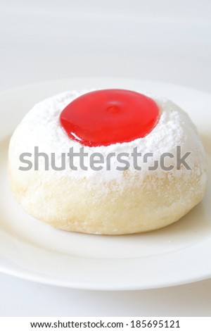 Donut with strawberry jam on white dish.