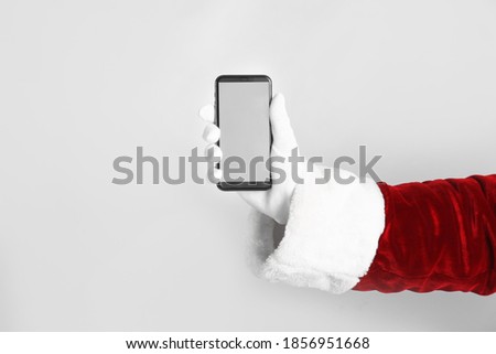 Santa holding modern mobile phone with blank screen on light grey background, closeup. Space for text