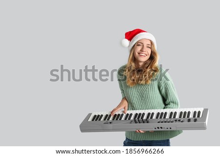 Young woman in Santa hat playing synthesizer on light grey background, space for text. Christmas music