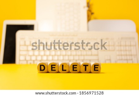 The word delete written with dices in front of a yellow background with computers and keyboard