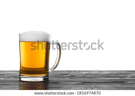 Glass mug of tasty beer on black wooden table against white background