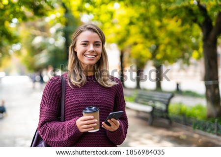 Beautiful smiling mixed race girl reading message or browsing her mobile phone while having coffee break outdoors.