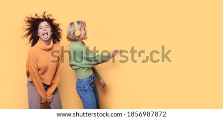 Charming two women dancing on a yellow wall with free space while listening to music