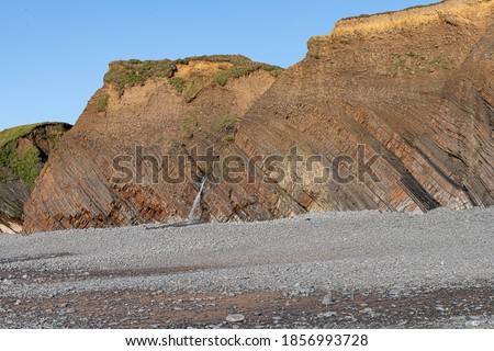 looking across pebbly beach to sedimentary rocks Royalty-Free Stock Photo #1856993728