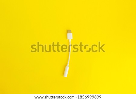 Adapter for a USB - 3.5 mm type c headphone cable on a smartphone. Close-up of a white 3.5 mm audio cable on a yellow isolated background. Copy space. The view from the top