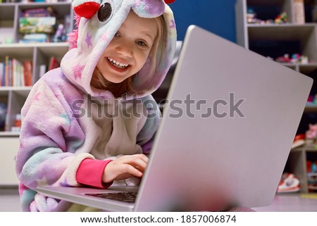Little girl in pajama unicorn lying at home on the wooden white floor with a laptop. Children's working with a laptop distance education. self-isolation
