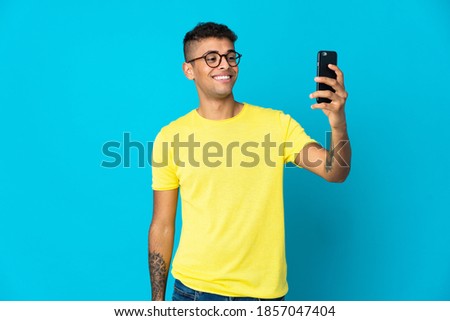 Young Brazilian man isolated on blue background making a selfie
