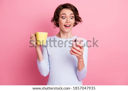 Positive astonished girl hold mug beverage use smartphone wear white jumper isolated pastel color background