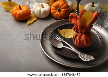 Seasonal table setting with pumpkins and autumn leaves on grey background. Space for text
