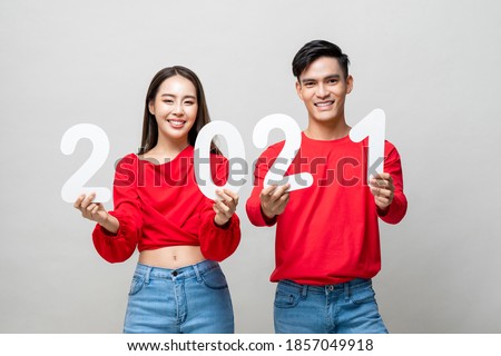 Happy Asian couple smiling and showing number 2021 for new year concept on light gray studio background