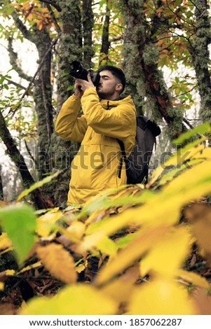 young student boy making a photo among yellow leaves in the forest with yellow autumnal coat