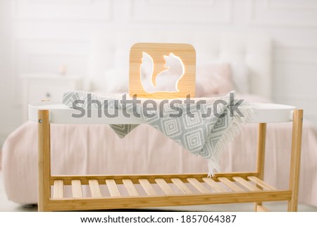 Wooden lapms and decor details at home interior. Stylish wooden hand made lamp with fox cut out picture, on little coffee table, standing in light home bedroom