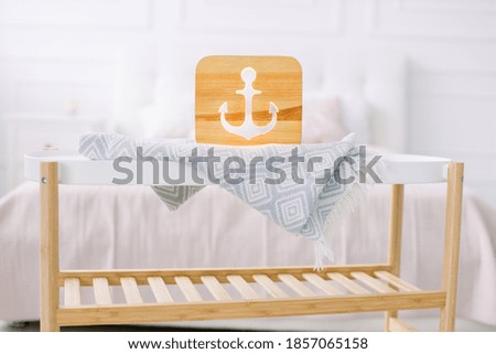 Wooden lapms and decor details at home interior. Stylish wooden hand made lamp with anchor cut out picture, on little coffee table, standing in light home bedroom