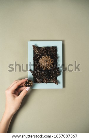 Female hands make a picture from pine cones and blue photo frames