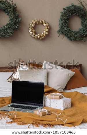 Laptop with blank screen on bed in stylishly decorated for Christmas holidays bedroom.