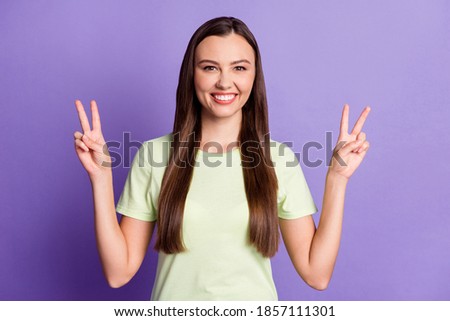 Portrait of funny young woman show two hands fingers v-sign light green clothing isolated on purple color background