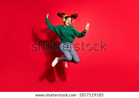 Full length photo of adorable young lady wear green knitted pullover listening music headphones dancing jumping isolated red color background