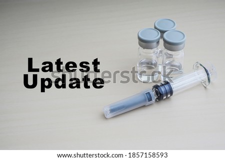 LATEST UPDATE text with Syringe and vials on wooden background. Coronavirus or Covid-19 Vaccine concept