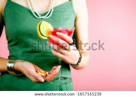 Studio photo of elegant woman in green dress with drink in one hand, and pills or drugs in other hand. Addiction concept.
