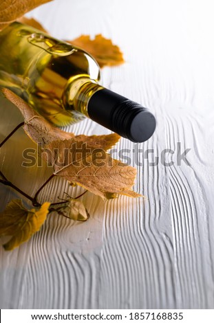 An unopened bottle of white wine and grapevine on an old wooden background. Wine on a white table. Copy space.