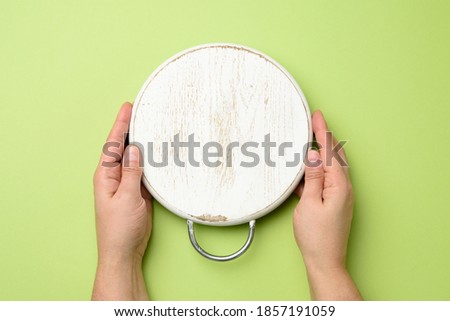 woman hand holding white empty round wooden board in hand, green background, top view