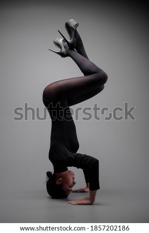 long-legged girl dancer in a black bodysuit and stockings in a photo studio in unusual poses on a gray background