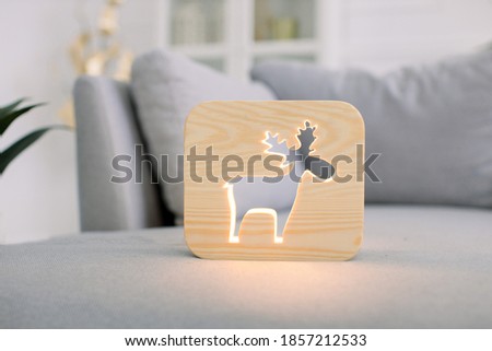 Close up of wooden night lamp with deer picture, at stylish light home living room interior, on gray modern sofa. Home decor, lamps and accessories