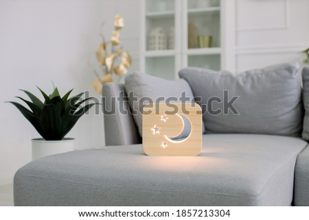 Wooden hand made accessories. Wooden night lamp with moon and stars picture, on gray sofa, at stylish light home living room interior. Home decor and lamps.