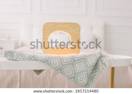 Close up of cozy wooden night lamp with hedgehog cut out picture, on gray blanket at cozy light bedroom interior. Wooden decorations and accessories at home interior