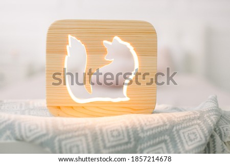Close up of cozy wooden night lamp with fox cut out picture, on gray blanket at cozy light bedroom interior. Wooden decorations and accessories at home interior