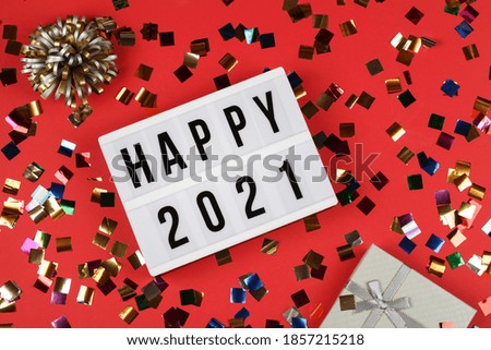 white lightbox with words happy 2021, gift box and holiday confetti on red background. top view. New year celebration. Happy New Year 2021 concept. 